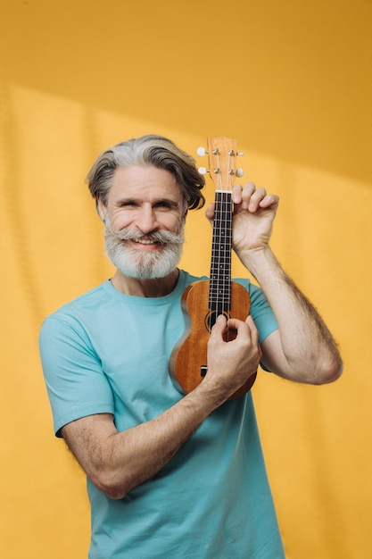 Studio portrait of senior retired elderly man playing ukulele