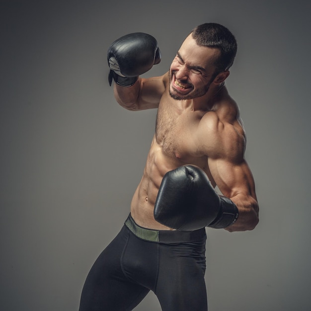 Studio portrait of shirtless male fighter in boxing gloves.