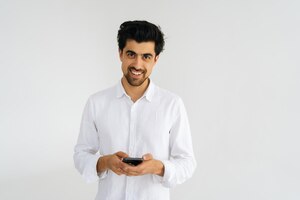 Studio portrait of smiling young man in casual shirt looking at camera holding smartphone using online mobile apps