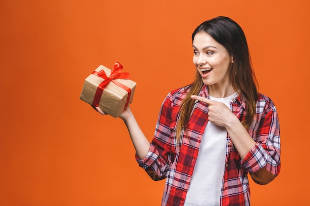 Studio portrait of smiling young  woman holds red gift box. Isolated against orange background.