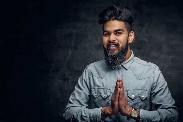 Studio portrait of stylish bearded Indian man in a blue shirt over grey background.