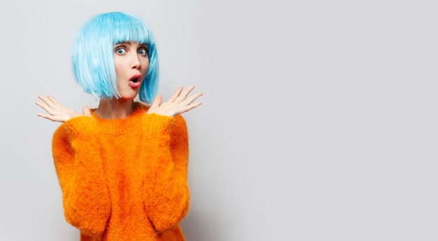 Studio portrait of surprised girl with blue wig, isolated on grey wall.