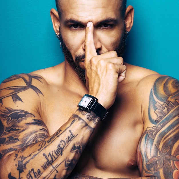 Studio portrait swarthy tanned man with a muscular body and tattoos looks directly into the camera