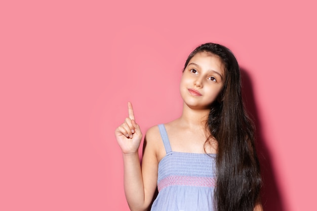 Studio portrait of thoughtful teenage girl, looking and showing up with finger, having new idea