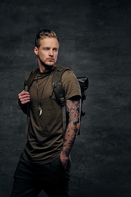 Studio portrait of urban style backpacker in Camo green t shirt and tattoos on arms.