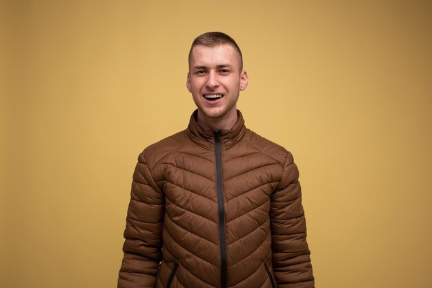 Studio portrait. Young 20s man in a brown jacket, on a yellow background, looks surprised