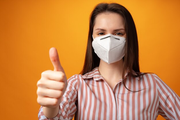 Studio portrait of a young beautiful woman wearing medical face mask against yellow background