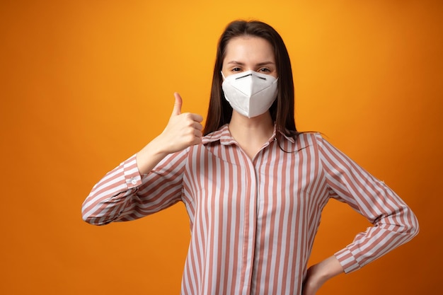 Studio portrait of a young beautiful woman wearing medical face mask against yellow background