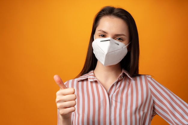 Studio portrait of a young beautiful woman wearing medical face mask against yellow background