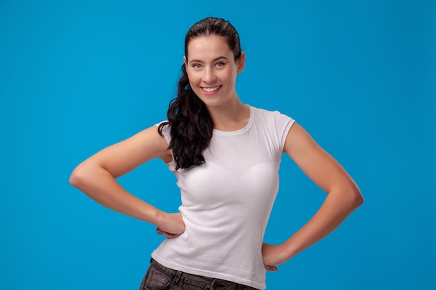 Studio portrait of a young beautiful woman in a white t-shirt against a blue wall background. People sincere emotions.