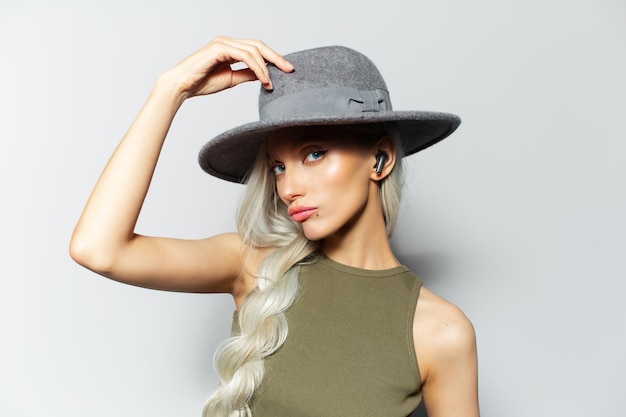 Studio portrait of young blonde attractive girl with earbuds in ears on white background wearing grey hat