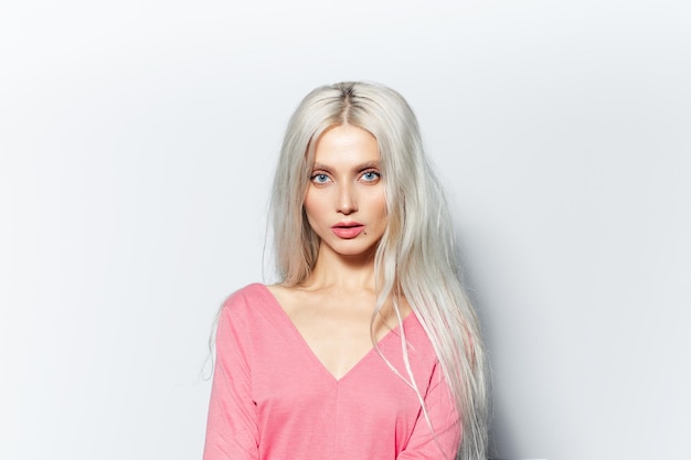 Photo studio portrait of young blonde pretty girl wearing pastel pink shirt on white background