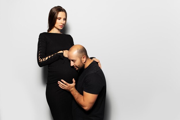 Studio portrait of young couple future parents Pregnant woman young father touching the belly of his wife on white background Wearing black