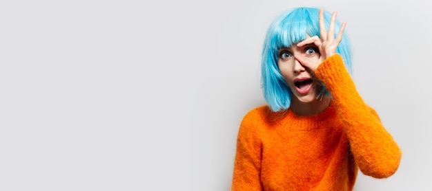 Studio portrait of young girl gesturing ok sign on the white background. Wearing orange sweater and blue wig bob. Panoramic banner view with copy space.
