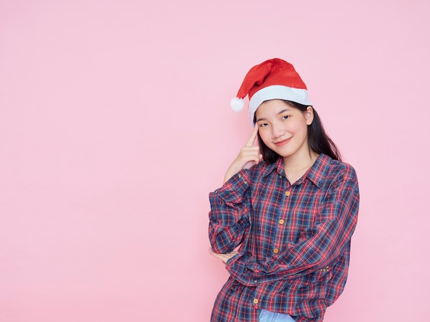 ピンクの背景にサンタの帽子をかぶっている少女のスタジオポートレート。クリスマスのコンセプト。