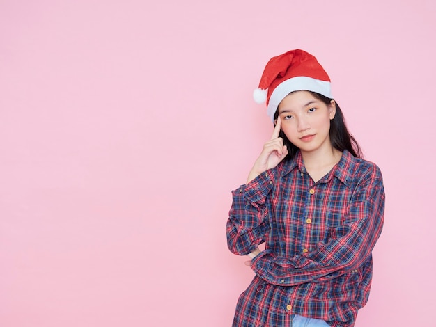 분홍색 배경에 산타 모자를 쓰고 젊은 여자의 스튜디오 초상화. 크리스마스 컨셉입니다.
