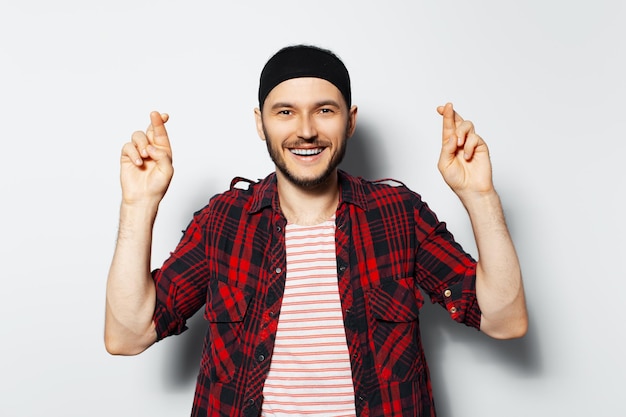 Studio portrait of young handsome happy man with crossed fingers wearing red plaid shirt on white background