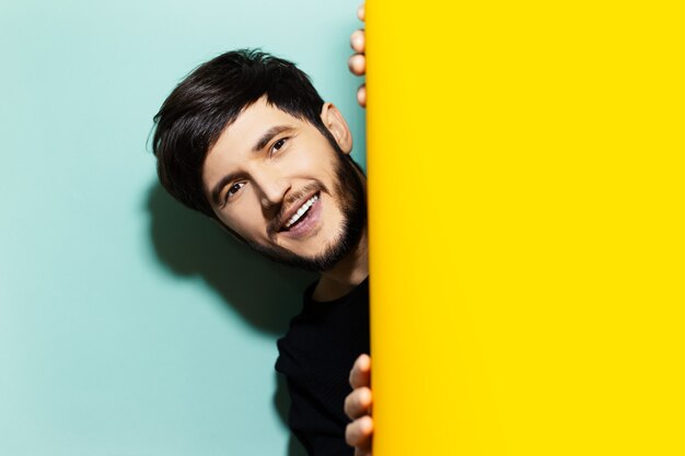 Studio portrait of young happy guy between two backdrops of yellow and aqua menthe colors.