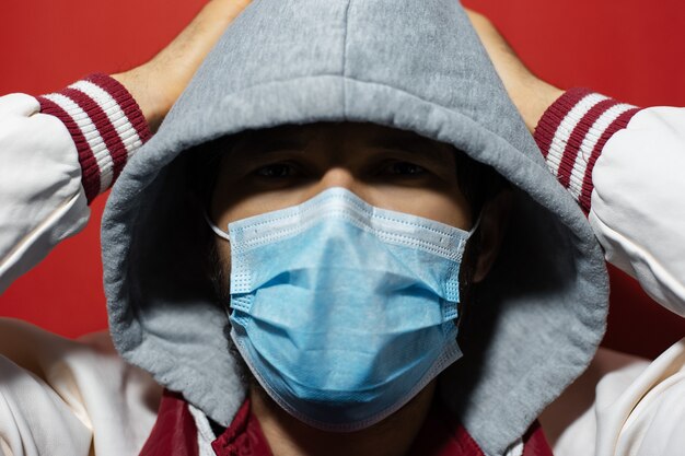 Photo studio portrait of young hooded guy wearing medical flu mask