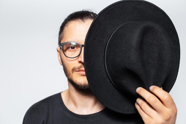 Studio portrait of young man hides half face with black hat on white
