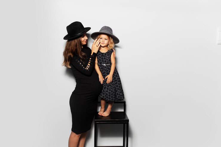 Studio portrait of young pregnant woman with her daughter on white background Wearing hats dressed in black