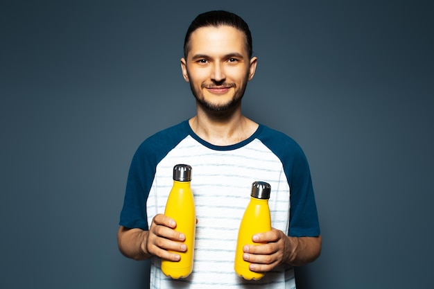 Studio portrait of young smiling guy with two yellow eco bottles in hands