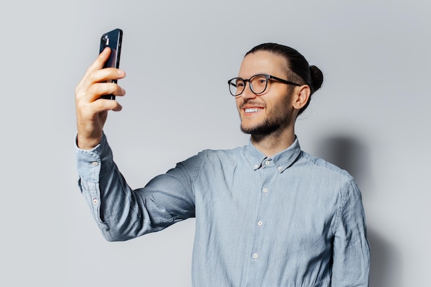 흰색 바탕에 스마트폰으로 셀카 사진을 만드는 웃고 있는 젊은 남자의 스튜디오 초상화