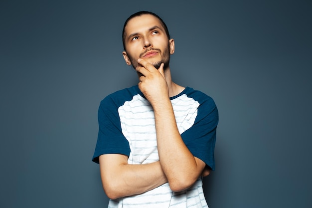 Studio portrait of young thoughtful man looking up with hand under chin on blue background