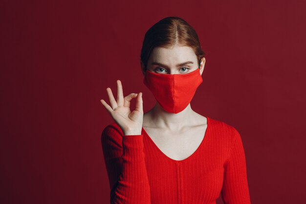 Studio portrait of young woman in protective medical face mask isolated on red background. Yoga, calm, zen and meditation a covid-19 pandemia concept