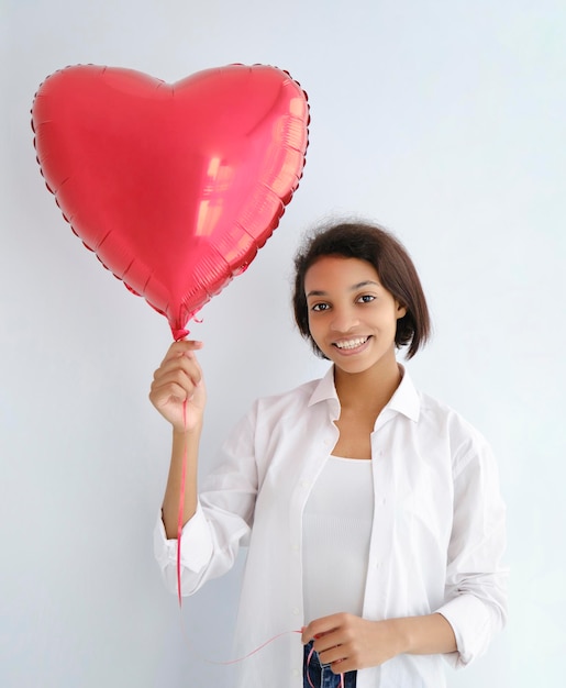 Studio portrait of young woman with dark skin the festive red wall with heart shaped balloon Close up isolated background copy space