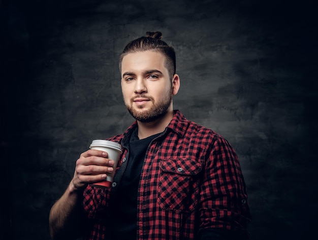 Studio portret van bebaarde hipster man gekleed in een fleece shirt houdt papieren kopje koffie.