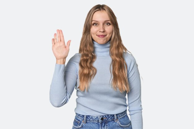 Studio portret van een blonde blanke vrouw die vrolijk glimlacht en nummer vijf met vingers toont