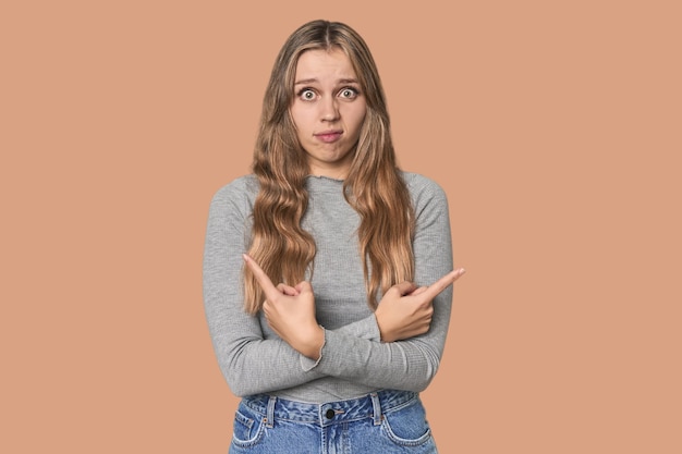 Foto studio portret van een blonde blanke vrouw wijst zijwaarts probeert te kiezen tussen twee opties