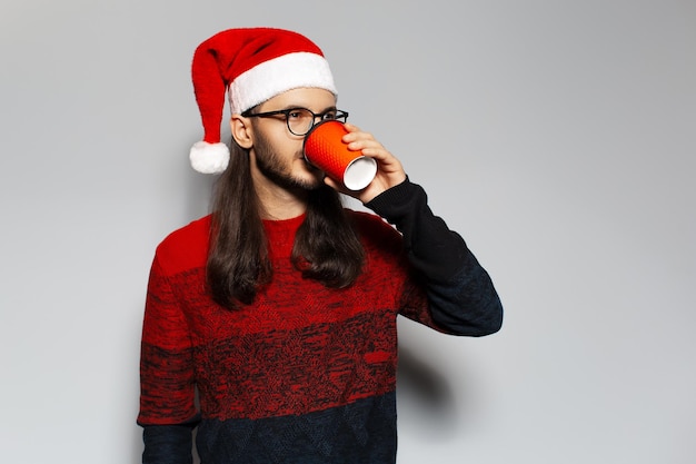 Studio portret van een knappe lachende man die koffie drinkt uit een papieren beker met een kerstmuts op een witte achtergrond