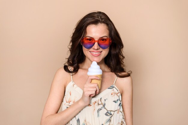 Studio portret van een vrolijke vrouw met een brede glimlach in een zomerjurk met een ijsje geïsoleerd op een beige achtergrond met vrije ruimte voor uw promotionele inhoud Vrije tijd concept