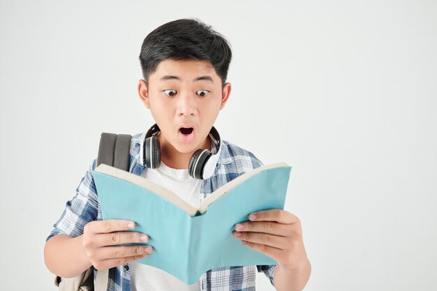 Studio portret van geschokt opgewonden schooljongen met rugzak lezen tekst in boek