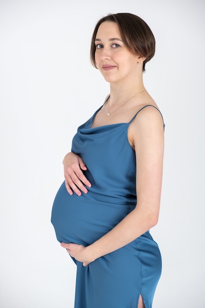 Studio portret van jonge volwassen zwangere vrouw in blauwe jurk op witte grijze muur, gelukkig zwangerschap concept