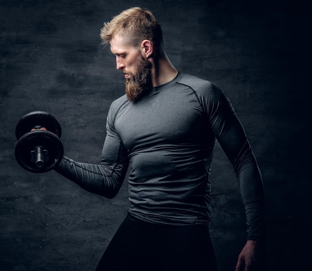 Studio portret van sportieve bebaarde man gekleed in een grijze sportkleding houdt halter.