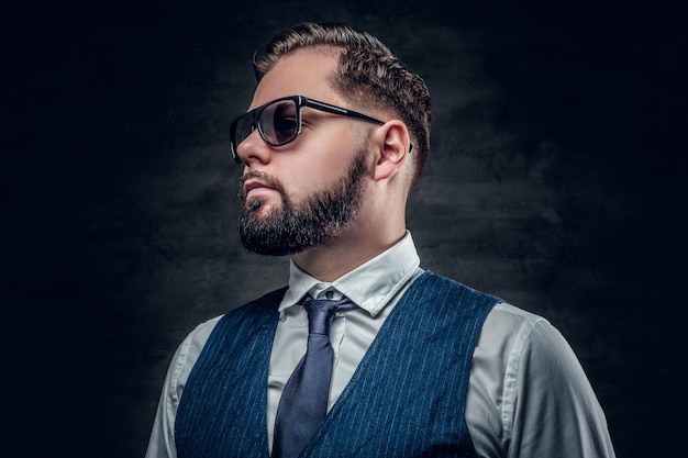 Studio portret van stijlvolle bebaarde zakenman in zonnebril met vest en vlinderdas.