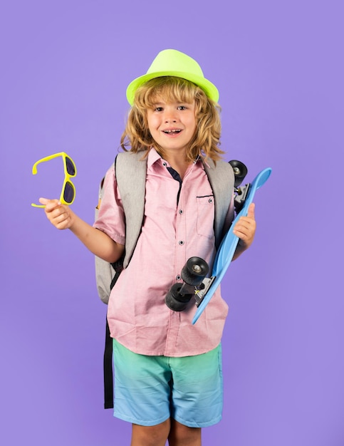 Studio portret van stijlvolle schattige jonge kindjongen met skateboard geïsoleerd tegen blauwe achtergrond Kid skater Jeugd en gelukkige tijd Schattig kind met skateboard en rugzak