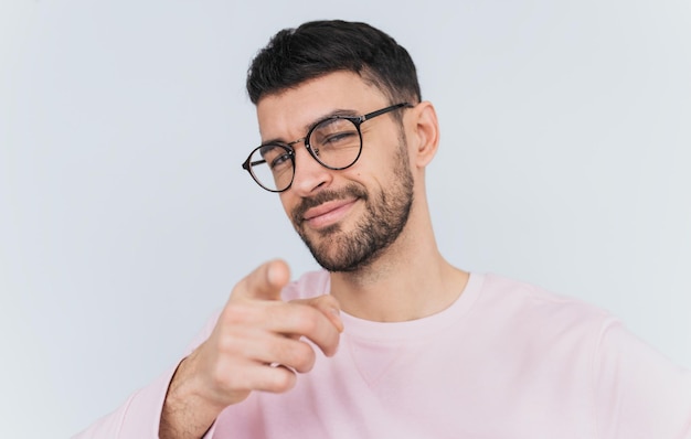 Studio portret van tevreden man draagt roze trui wijst naar je kiest iemand of adverteert product Knappe lachende man geeft aan op camera geïsoleerd op witte muur achtergrond