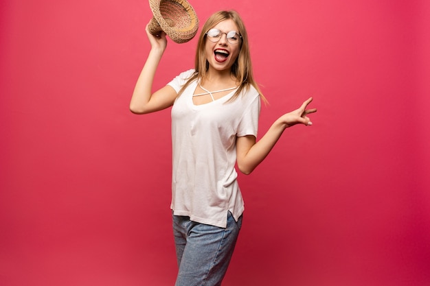 Studio portret van vrolijk vrouwelijk model zomer hoed houden en glimlachen. Blond meisje in zonnebril en wit overhemd plezier tijdens fotoshoot.