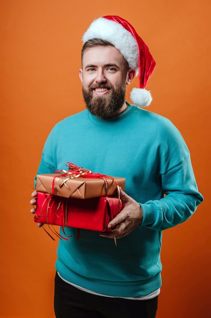 Foto riprese in studio, un ragazzo con un maglione blu con regali di capodanno tra le mani su uno sfondo arancione