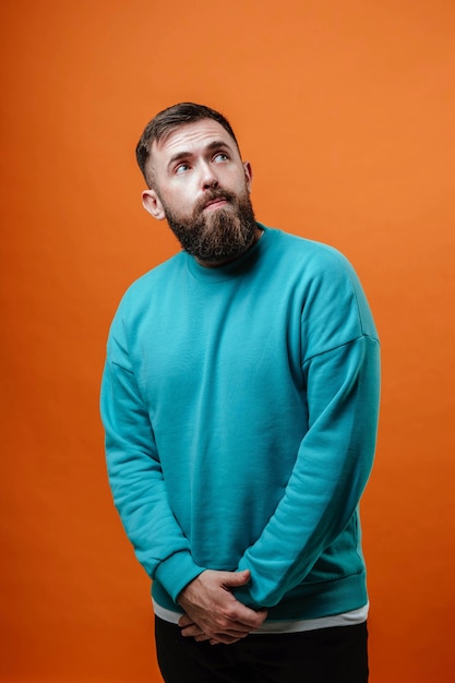 Photo studio shooting, a young bearded guy on an orange background looks up