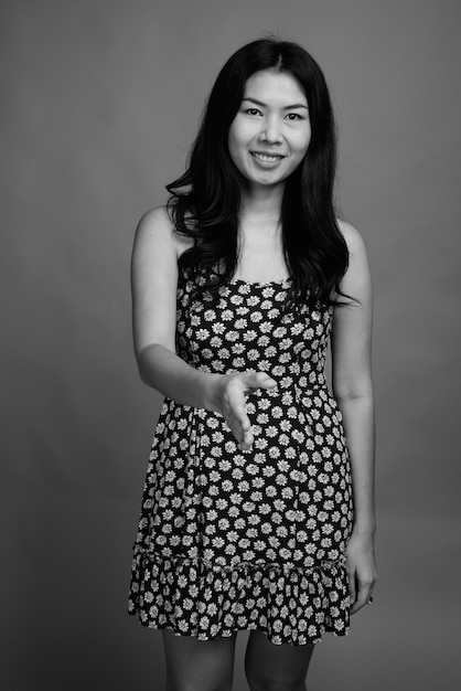 Studio shot of Asian woman wearing dress against gray background in black and white