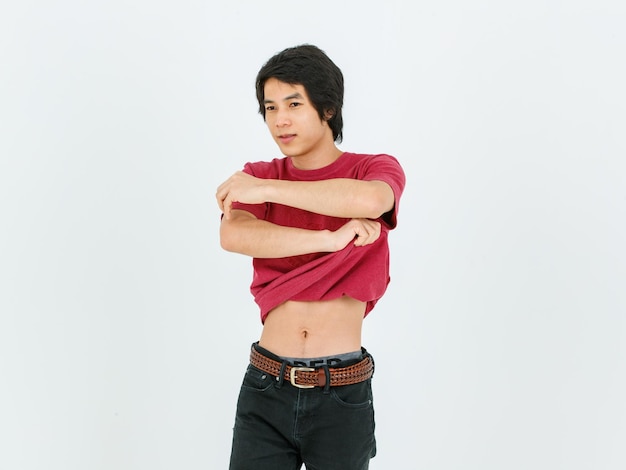 Studio shot of Asian young handsome confident slim teenager male model in casual street style outfit standing holding hands taking stripping t shirt off showing muscular abdomen on white background