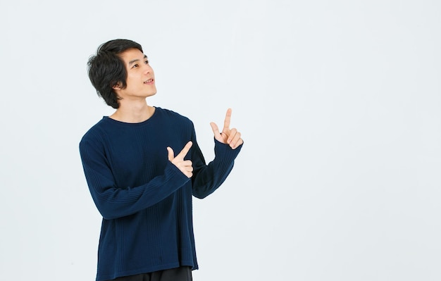 Studio shot del giovane modello maschile asiatico bello sottile adolescente moda in camicia a maniche lunghe in piedi sorridente tenendo le mani puntando le dita sullo spazio vuoto della copia che presenta il prodotto su sfondo bianco