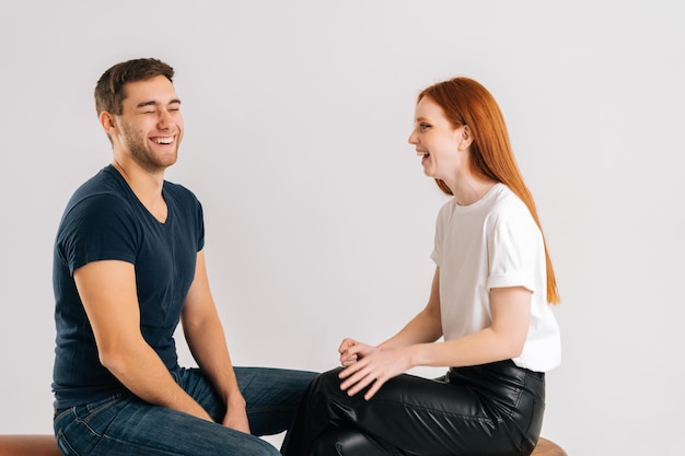 Studio shot of attractive cheerful young man and woman talking and laughing on white isolated background. Joyful young couple having pleasant conversation. People lifestyle concept.