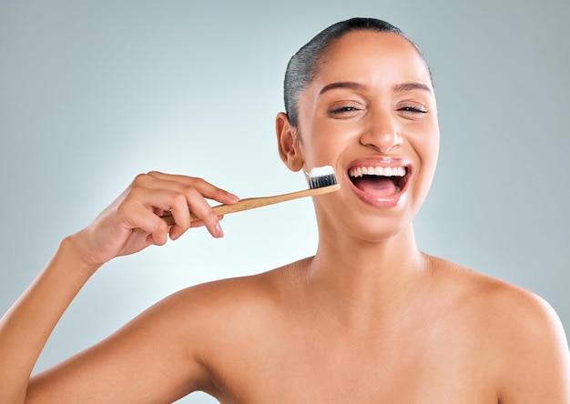 Studio shot of an attractive young woman brushing her teeth against a grey background