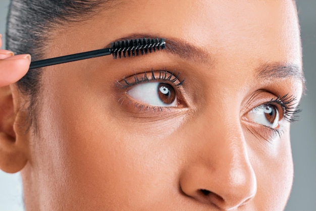 Photo studio shot of an attractive young woman putting on mascara against a grey background